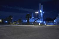 an empty parking lot next to a factory at night, lit up by street lights