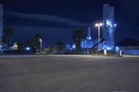 an empty parking lot next to a factory at night, lit up by street lights