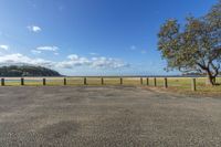 empty parking lot next to field with trees, and a lake in the background and blue sky