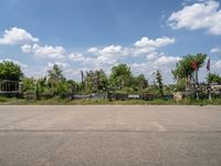 an empty parking lot with benches and flags in the distance, and some weeds in the background