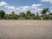 an empty parking lot with benches and flags in the distance, and some weeds in the background