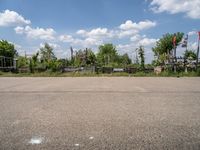 an empty parking lot with benches and flags in the distance, and some weeds in the background