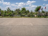 an empty parking lot with benches and flags in the distance, and some weeds in the background