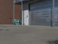 a empty parking lot near a garage door and brick wall wall and the road is paved in between it