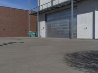 a empty parking lot near a garage door and brick wall wall and the road is paved in between it