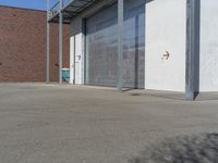 a empty parking lot near a garage door and brick wall wall and the road is paved in between it