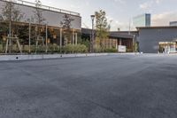 a paved, empty parking lot with a large glass building in the background and buildings and planters