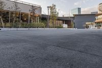 a paved, empty parking lot with a large glass building in the background and buildings and planters