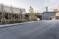 a paved, empty parking lot with a large glass building in the background and buildings and planters