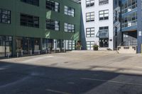 a large empty parking lot and a green building in the background with people walking up it