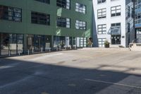 a large empty parking lot and a green building in the background with people walking up it