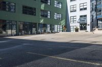 a large empty parking lot and a green building in the background with people walking up it