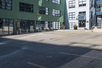 a large empty parking lot and a green building in the background with people walking up it