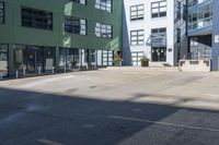 a large empty parking lot and a green building in the background with people walking up it