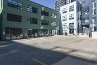 a large empty parking lot and a green building in the background with people walking up it