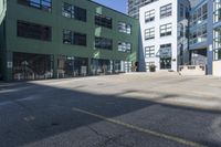 a large empty parking lot and a green building in the background with people walking up it