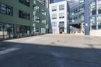 a large empty parking lot and a green building in the background with people walking up it