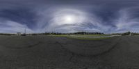 the wide lens of an empty parking lot shows a blue sky and some clouds in front of the sun