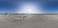 an empty parking lot on a clear day with some street lights in the background and traffic going by