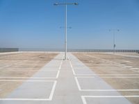 an empty parking lot with a line of street lights in front of it and a clear blue sky