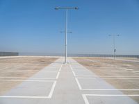 an empty parking lot with a line of street lights in front of it and a clear blue sky