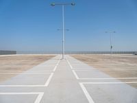 an empty parking lot with a line of street lights in front of it and a clear blue sky