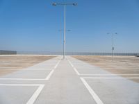 an empty parking lot with a line of street lights in front of it and a clear blue sky