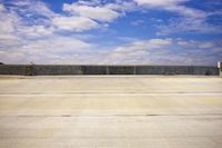 an empty parking lot in front of some buildings and water lines with a sky background