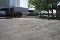 a train is passing by the empty parking lot by a large building and tree branches