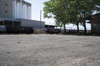 a train is passing by the empty parking lot by a large building and tree branches