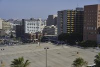 an empty parking lot in front of some tall buildings with palm trees in the foreground