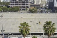 an empty parking lot in front of some tall buildings with palm trees in the foreground