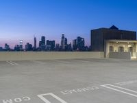 an empty parking lot with a cityscape in the background and a white arrow painted on it