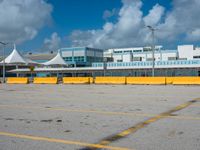 an empty parking lot filled with lots of buildings and trucks in the background of a cloudy blue sky