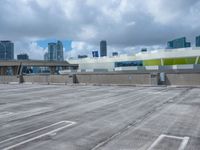 an empty parking lot with a parking garage below it in a big city, with a skyline visible in the background