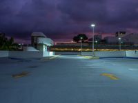 an empty parking lot lit up at night by street lights and purple sky above the buildings