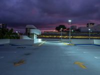 an empty parking lot lit up at night by street lights and purple sky above the buildings