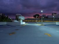 an empty parking lot lit up at night by street lights and purple sky above the buildings