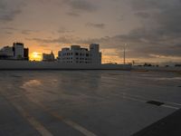 a empty parking lot with a sunset behind it and some buildings in the distance as the sun sets