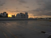 a empty parking lot with a sunset behind it and some buildings in the distance as the sun sets