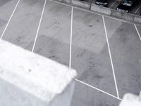 an empty parking lot with parking meters and parked cars visible in the background, looking down on the empty lot