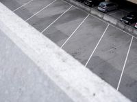 an empty parking lot with parking meters and parked cars visible in the background, looking down on the empty lot