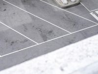 an empty parking lot with parking meters and parked cars visible in the background, looking down on the empty lot