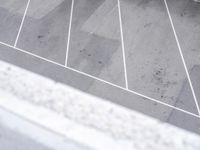 an empty parking lot with parking meters and parked cars visible in the background, looking down on the empty lot