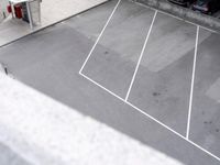 an empty parking lot with parking meters and parked cars visible in the background, looking down on the empty lot
