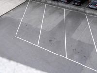an empty parking lot with parking meters and parked cars visible in the background, looking down on the empty lot