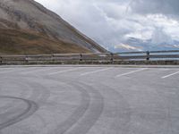 an empty parking lot by a mountain, with a motorcycle on one side and the other side painted black and white