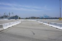 an empty parking lot with a naval ship in the background and a barge on the far side