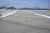 an empty parking lot with a naval ship in the background and a barge on the far side