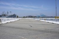 an empty parking lot with a naval ship in the background and a barge on the far side